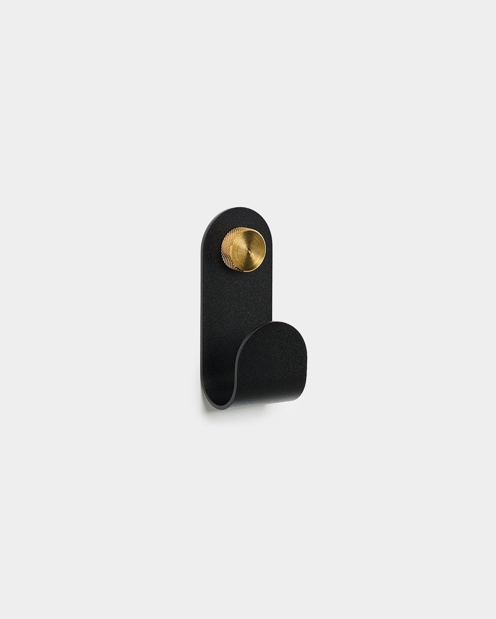 De Norr Single Hanger in black van WoodUpp, met een gebogen ontwerp en een rond brass accent, afgebeeld tegen een effen witte achtergrond.